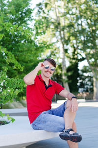 Young happy handsome bearded man, tourist sitting in green park. summer vacation. sunglasses.