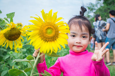 Portrait of girl gesturing while holding sunflower on field