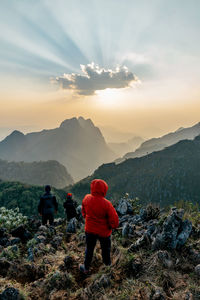 Rear view of men walking on mountain against sky during sunset