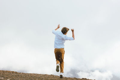 Rear view of boy jumping against sky