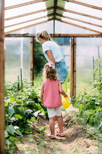 A happy little girl helps her mother to water the plants in the greenhouse. childhood, parenting