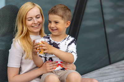 Happy blond woman and little boy sitting on terrace and eating sweets. mother and son enjoy 
