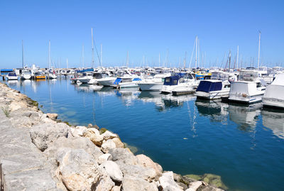 Sailboats moored on harbor against clear blue sky