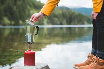 Low section of person making coffee against lake