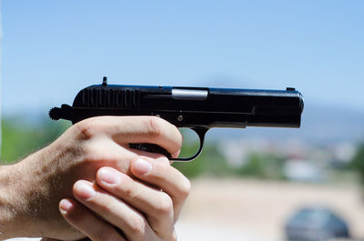 Cropped hands holding gun against clear sky