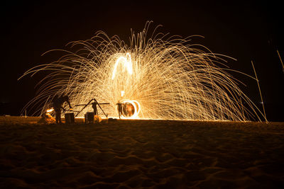 Illuminated ferris wheel on beach against sky at night