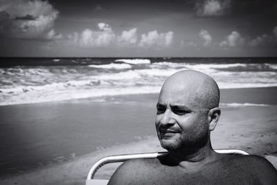 Thoughtful man looking away while sitting at beach against sky