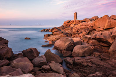 Rocks on sea shore against sky during sunset