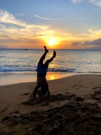 Silhouette man doing handstand at beach during sunset