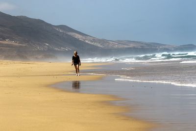 Woman walking on beach against sky