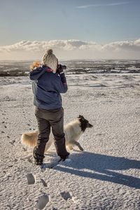 Rear view of person standing with dog on snowy field against sky