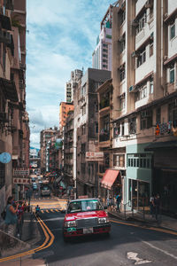 Vehicles on road by buildings in city against sky