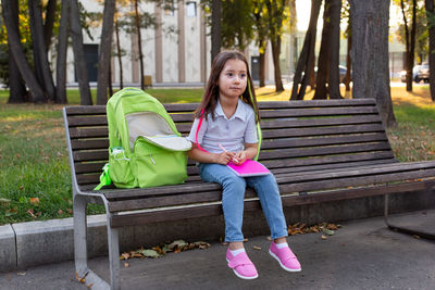 Thoughtful girl with backpack resting on park bench in autumn setting