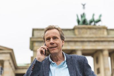 Portrait of smiling senior man on the phone at brandenburg gate, berlin, germany