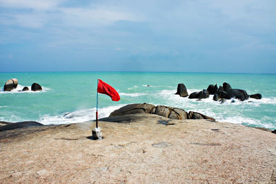 Red flag standing on rocky coast of gulf of thailand against the backdrop of the blue sea and sky