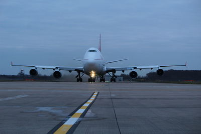 Airplane on runway against sky at dusk