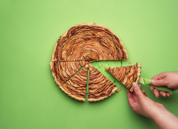 Cropped hand holding apple pie on green background