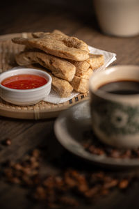 Keropok lekor or fried fish cake on a rattan plate with a sweet chilli sauce and on wooden table. 