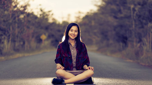 Portrait of smiling young woman sitting on road
