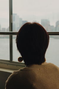 Rear view of woman looking through window while traveling in ferry