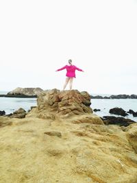 Rear view of woman standing on rock by sea against clear sky