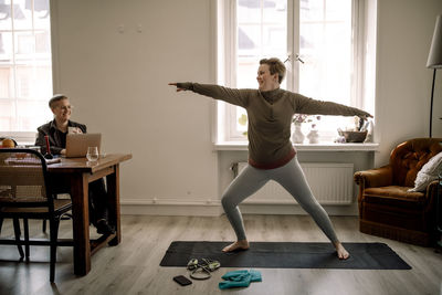 Smiling lesbian woman looking at girlfriend practicing yoga on mat