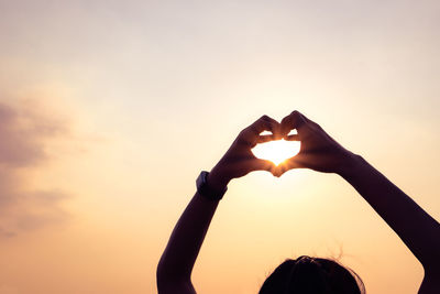 Hands forming a heart shape with sunset silhouette