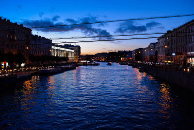 River amidst illuminated buildings against sky at dusk