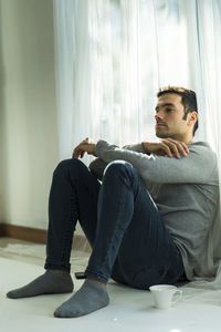 Depressed man with coffee cup sitting by window at home