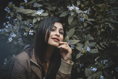 Portrait of beautiful young woman against white flowering plants