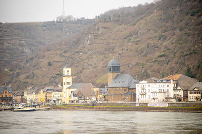 Buildings by river against mountain