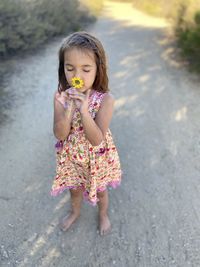 Full length of cute girl holding flower while standing outdoors