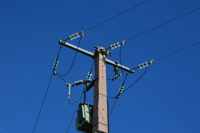 Low angle view of electricity pylon against clear blue sky