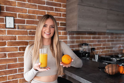Smiling young woman holding drink against brick wall