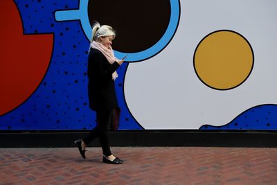 Side view of young woman using phone by colorful graffiti wall