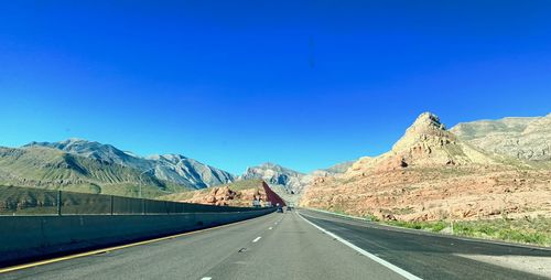 Road leading towards mountains against clear blue sky