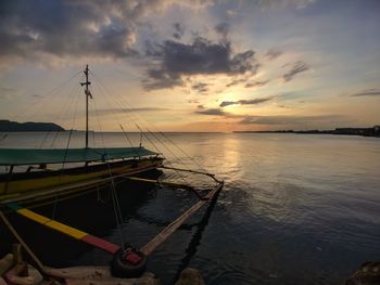 Sailboats moored on sea against sky during sunset