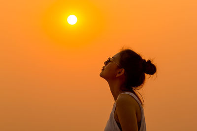 Side view of young woman against sky during sunset