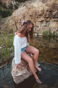 Woman sitting on rock against water