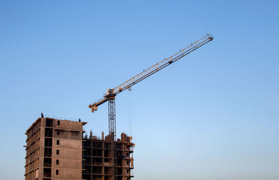 Low angle view of crane by building against clear blue sky