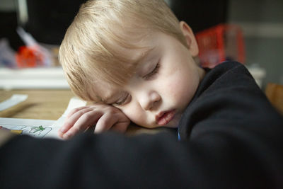 Close-up of cute toddler boy asleep with head leaning on arm at table