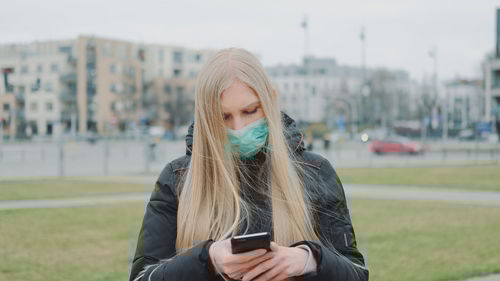 Young woman wearing mask using mobile phone in city