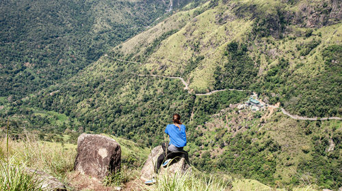 Rear view of woman sitting on rock at cliff