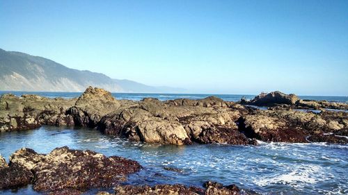 Rocks by sea against clear blue sky