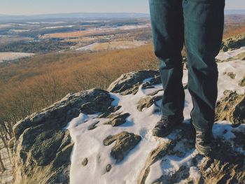 Low section of man standing on cliff with snow during winter