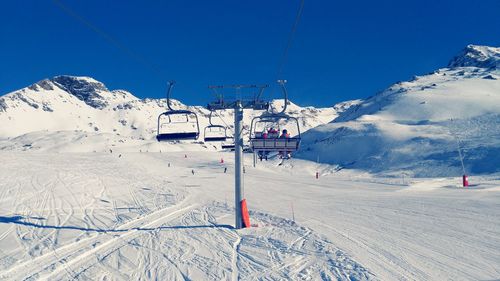 Ski lifts over snowy field against mountains and sky on sunny day