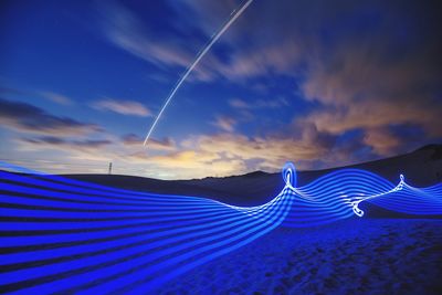 Illuminated blue light painting on sandy beach during sunset