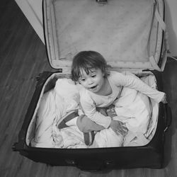 High angle view of playful girl sitting in suitcase