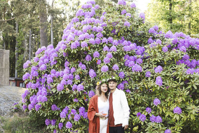 Portrait of mother and son wearing tiaras against flower plants at back yard during swedish summer solstice