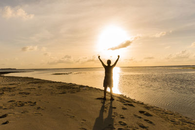 Silhouette woman standing on beach against sky during sunset